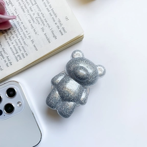 Macro detail of silver glitter bear phone grip with reflective resin finish on white desk