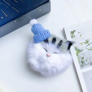 Close-up of white plush cat phone stand with blue knit hat and pompom detail