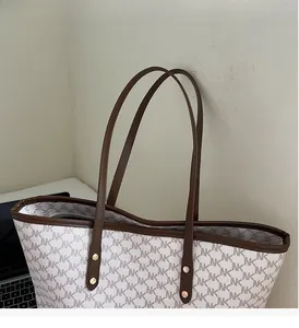Close-up of white monogram tote bag handle with brown leather trim and gold studs