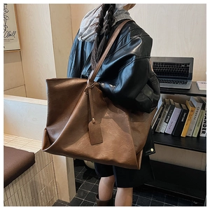 Brown large-capacity leather tote bag worn by a model in a minimalist study setting
