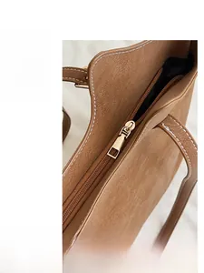 Detail view of the smooth metal zipper and white stitching on a brown suede tote bag