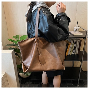 Brown textured leather tote bag with long strap and charm tag shown on a female model