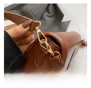 Close-up of golden metal hook on brown lychee texture leather shoulder bag strap