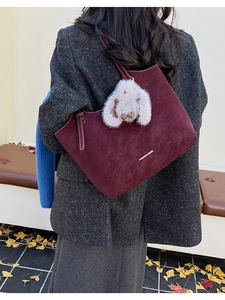 Detail of dark burgundy suede tote bag with plush rabbit charm and white text print