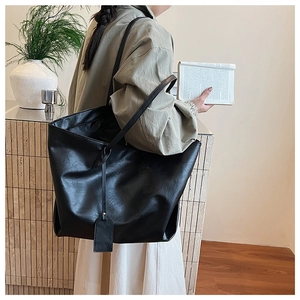 Detailed view of the large black leather tote bag worn by a model in a cozy indoor setting