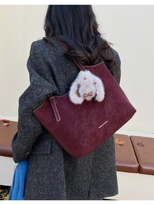 Detail of burgundy suede tote bag with plush rabbit charm on autumn tweed coat
