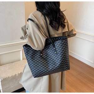 Detail of grey monogram tote bag with NK pattern and black leather straps on a trench coat