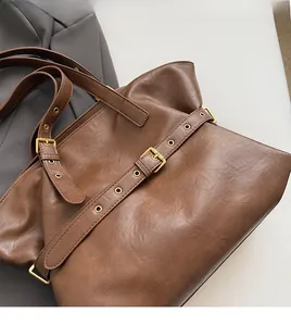 Macro detail of dark brown leather tote showing textured finish and golden buckle hardware