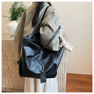 Detail of a large matte black leather tote bag with a sleek minimalist tag and long strap