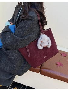 Detail of burgundy tote bag with plush bunny charm and printed logo text in autumn setting