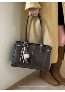 Sac cabas rétro en cuir marron foncé avec breloques porté par un mannequin en tenue d'automne