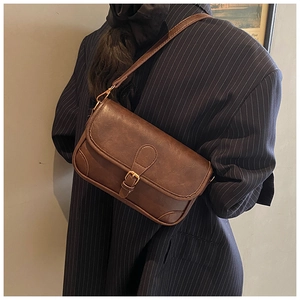 Macro detail of dark brown vintage crossbody bag with metallic buckle on navy blazer