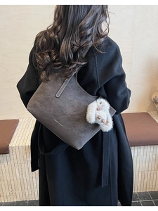 Detail of dark grey tote bag with fluffy rabbit charm on a stylish wool coat