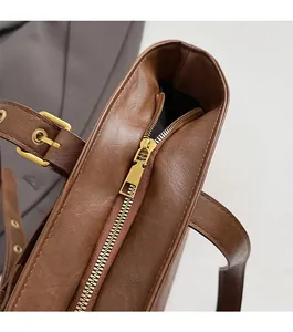 Detail view of smooth golden metal zipper and brown leather texture on a tote bag
