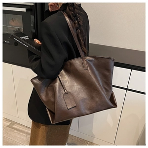 Side view of dark brown faux leather tote bag worn by model in a modern interior setting