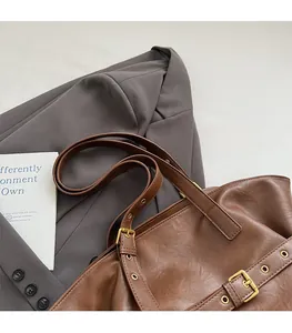Detail of dark brown leather tote bag with vintage gold buckle on a grey suit
