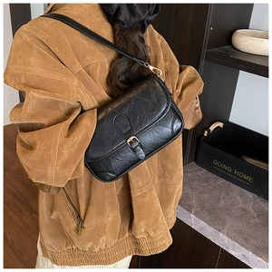 Detail of a vintage black leather shoulder bag featuring a metallic buckle and textured finish