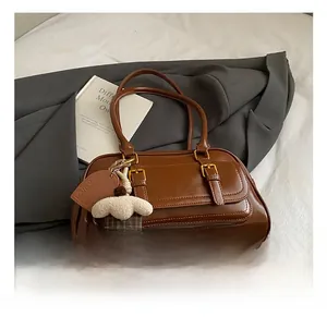 Detail of a brown leather Boston bag with a white fluffy charm and golden hardware