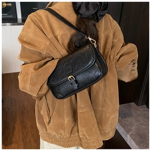 Retro black leather crossbody bag with gold buckle shown on shoulder from side view