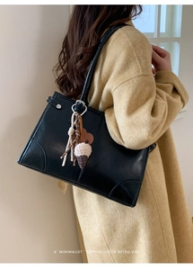 Sac à épaule en cuir noir avec breloques porté sur un manteau en laine jaune chaud