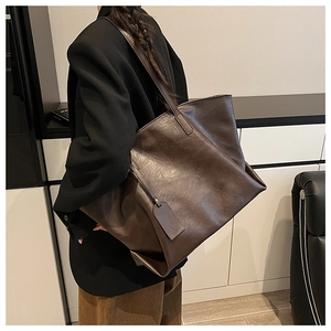 Side view of a dark brown large tote bag with leather texture worn by a model