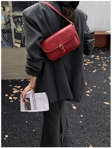 Street style view of a bright red leather crossbody bag with golden metal buckle clasp