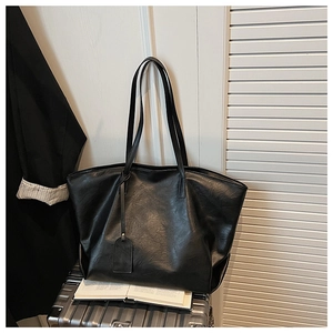 Minimalist black leather tote bag placed on a silver suitcase in a travel business setting