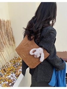 Brown suede tote bag with plush rabbit charm shown in a warm autumn outdoor setting