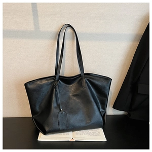 Detail of a black oversized tote bag with matte texture and minimalist hangtag on books