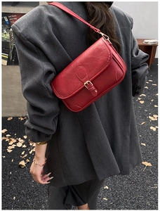 Retro red leather crossbody bag detail with gold buckle and荔枝 texture on grey suit