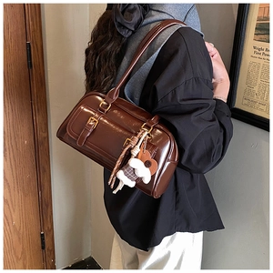 Detail of dark brown patent leather shoulder bag with plush charm and metal buckle