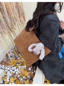 Detail of brown faux suede tote bag with white plush rabbit charm and fashion logo