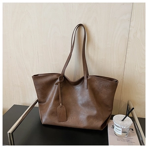 Detail of dark brown textured leather tote bag with long straps and hanging tag