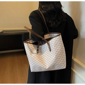 Detail of monogram tote bag with dual brown leather handles and zipper closure