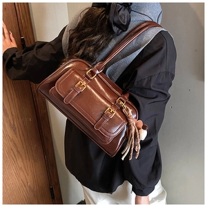 Caramel brown leather shoulder bag detail with twin metal buckles and bohemian tassel charm