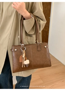 Détail du sac à bandoulière marron rétro avec breloque LOVELY sur sol en bois