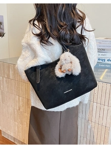 Detail of black tote bag with white contrast stitching and a plush rabbit charm