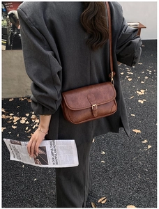 Close-up of vintage brown PU leather crossbody bag with golden buckle on autumn background