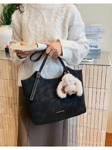 Detail of black suede tote bag with white stitching and plush bunny charm accessory