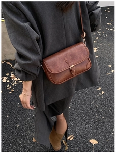 Close-up of a vintage brown crossbody bag with gold hardware worn over a grey blazer