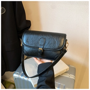Detail of black crossbody bag with vintage texture and gold metal buckle hardware
