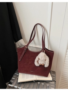 Detail of burgundy tote bag in matte suede with metal buckle and plush rabbit charm