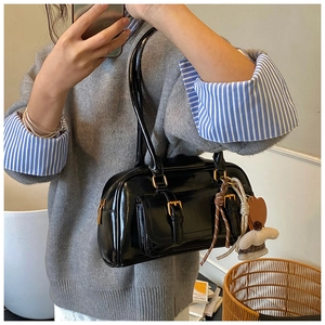 Detail of a chic black glossy leather underarm bag with gold hardware and heart charms