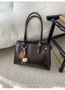 Détail d'un sac à bandoulière marron foncé brillant avec des breloques décoratives