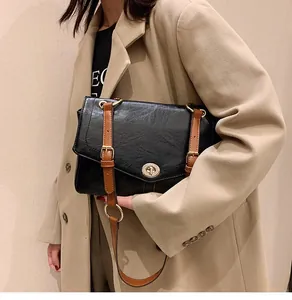 Détail du sac messager vintage en cuir noir avec boucles dorées et fermeture à verrou rotatif