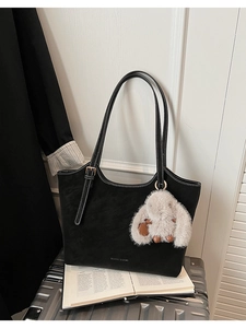 Detail of black suede tote bag with white contrast stitching and plush rabbit charm