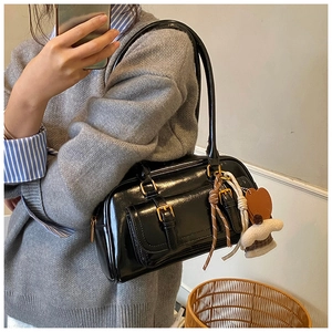 Close-up of black patent leather underarm bag with decorative charms and side pocket