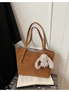 Detail of caramel brown tote bag with plush bunny charm on a silver suitcase
