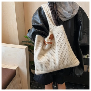 Detail of knit tote bag featuring hollow crochet pattern and brown leather toggle button