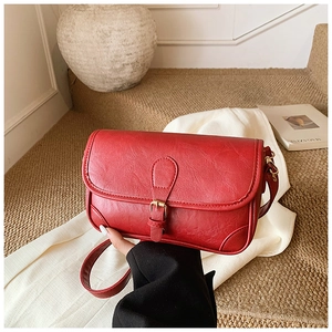 Close-up of red pebbled leather shoulder bag with buckle detail on white fabric
